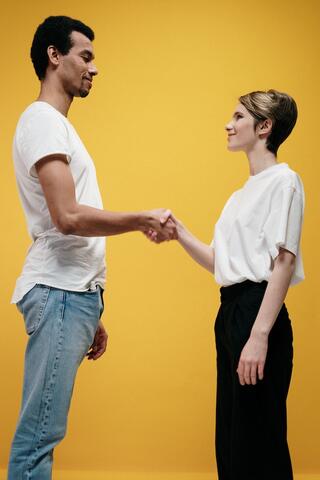 A man and a woman shaking hands in front of a yellow background
