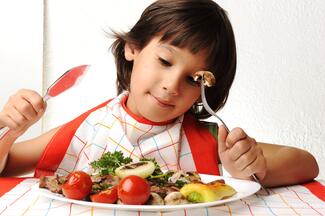 A child with a smile on his face holding utensils and eating salad